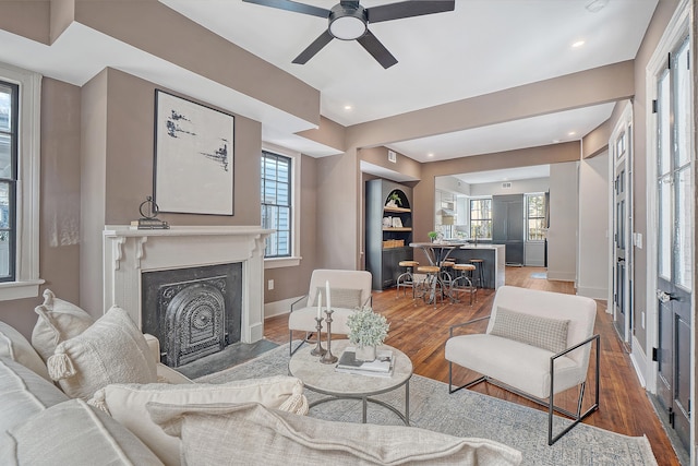 living room featuring a ceiling fan, a fireplace with flush hearth, wood finished floors, and baseboards