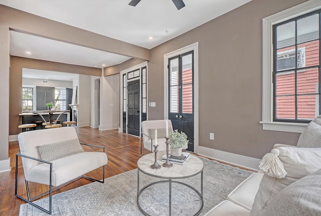 living area with a ceiling fan, wood finished floors, and baseboards