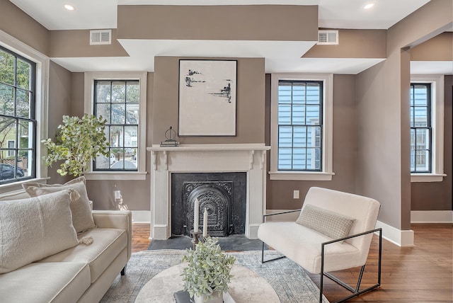 living area with a fireplace with flush hearth, wood finished floors, visible vents, and baseboards