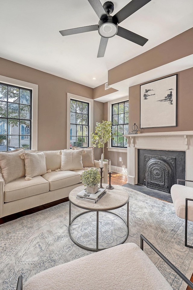 living room featuring baseboards, a fireplace with flush hearth, and ceiling fan