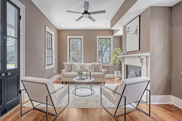 living area featuring ceiling fan, baseboards, wood finished floors, and a fireplace