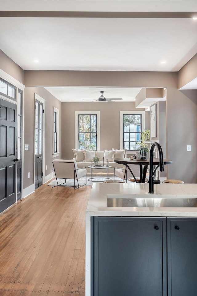 kitchen with light wood-style flooring, a ceiling fan, a sink, open floor plan, and baseboards