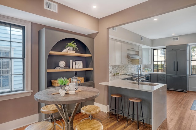 kitchen featuring visible vents, a kitchen bar, a peninsula, light wood finished floors, and light countertops