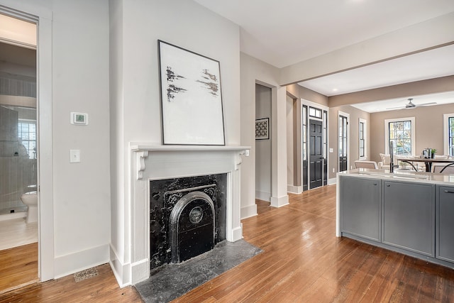 living area featuring a fireplace, baseboards, a ceiling fan, and wood finished floors