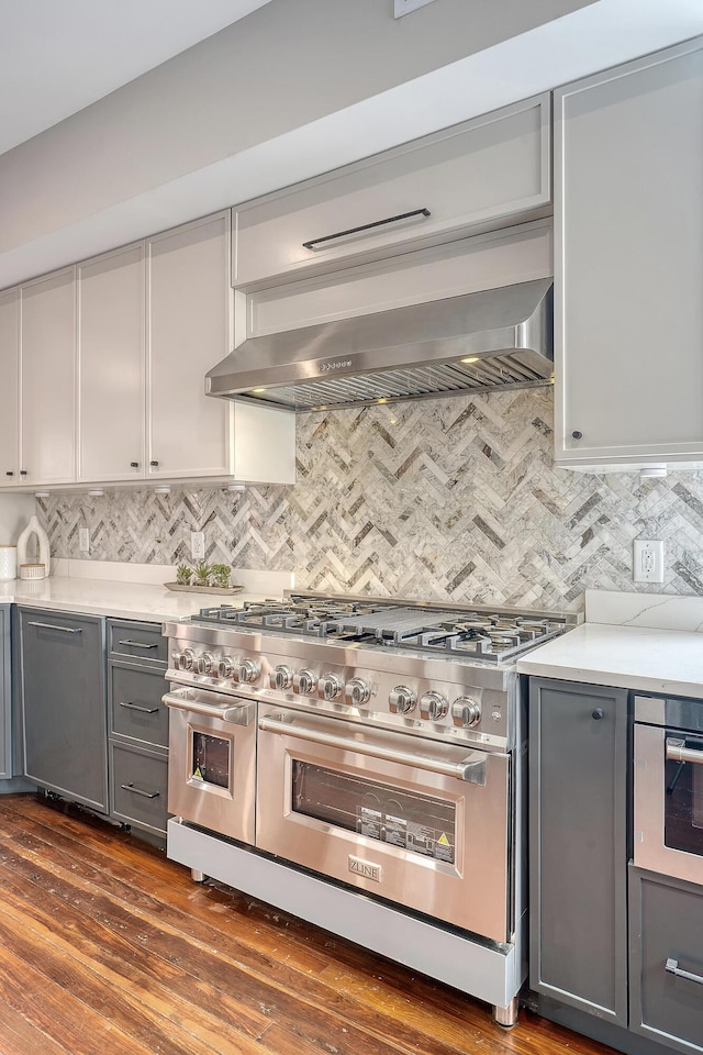 kitchen featuring tasteful backsplash, double oven range, wall chimney exhaust hood, and gray cabinetry