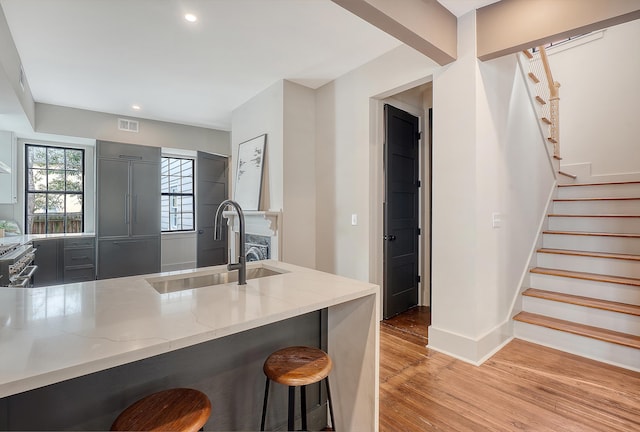 kitchen featuring light stone countertops, a sink, light wood-style floors, a kitchen bar, and high quality appliances