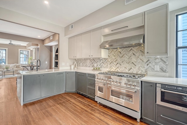 kitchen featuring gray cabinets, double oven range, a peninsula, wall chimney exhaust hood, and light countertops