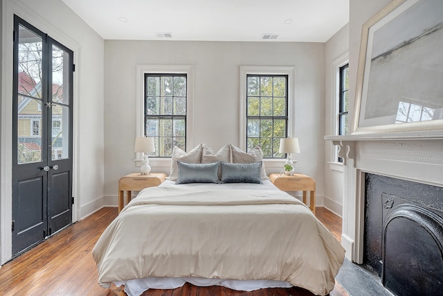 bedroom with a fireplace, wood finished floors, visible vents, and baseboards