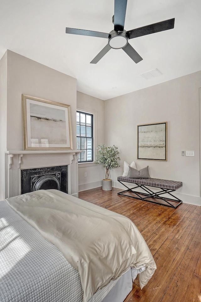 bedroom with visible vents, baseboards, a fireplace, hardwood / wood-style flooring, and a ceiling fan