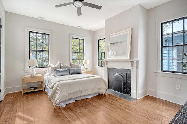 bedroom featuring visible vents, a fireplace with flush hearth, light wood-style floors, and baseboards