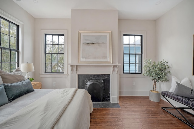 bedroom with a fireplace with flush hearth, baseboards, and wood finished floors