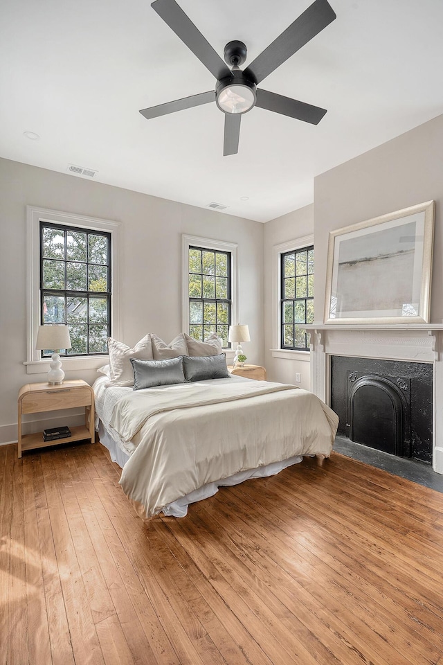 bedroom featuring ceiling fan, visible vents, a fireplace with flush hearth, and light wood-style flooring