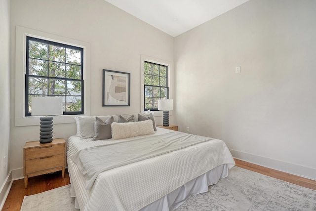 bedroom with wood finished floors, baseboards, and vaulted ceiling