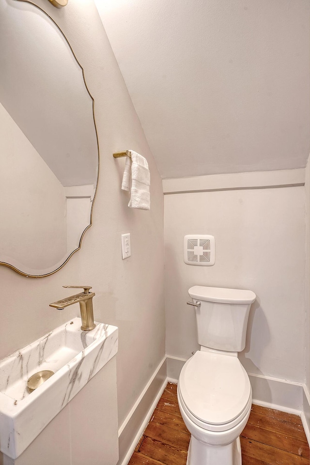 bathroom with vaulted ceiling, toilet, baseboards, and wood finished floors