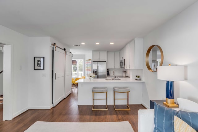 kitchen featuring a barn door, dark wood-style floors, a peninsula, and appliances with stainless steel finishes