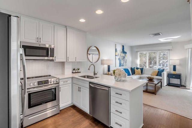 kitchen with visible vents, open floor plan, a peninsula, stainless steel appliances, and a sink