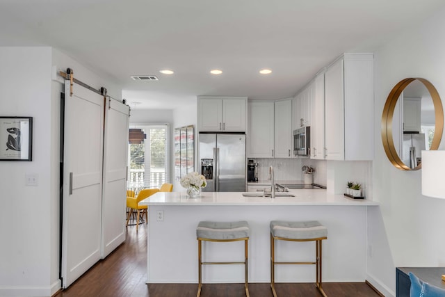 kitchen featuring a barn door, appliances with stainless steel finishes, a peninsula, white cabinets, and a sink