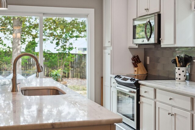 kitchen with light stone countertops, white cabinets, electric range, and sink