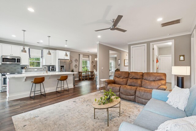 living room featuring ornamental molding, ceiling fan, a healthy amount of sunlight, and dark hardwood / wood-style flooring