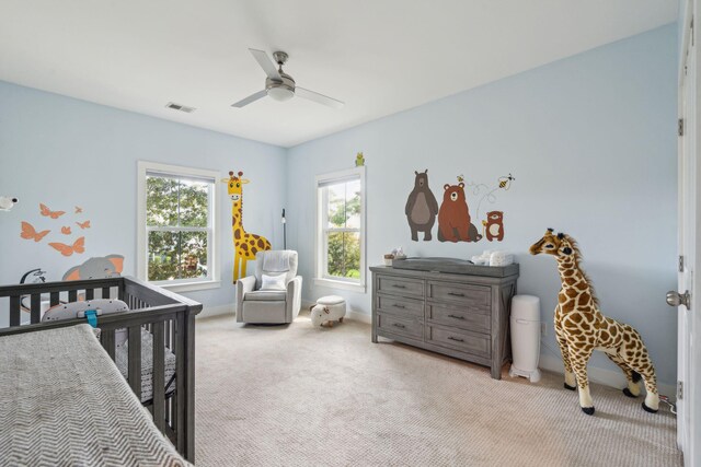 bedroom featuring light colored carpet, ceiling fan, and a nursery area