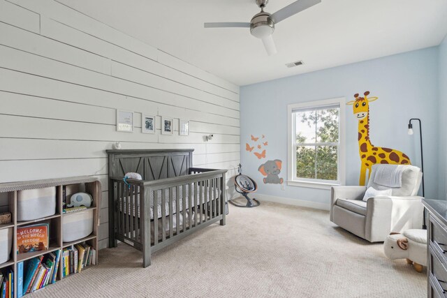 carpeted bedroom with ceiling fan and a nursery area