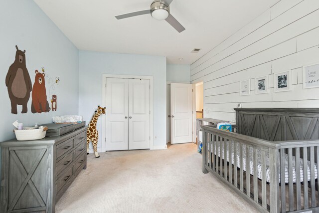 carpeted bedroom featuring a closet, ceiling fan, and a crib