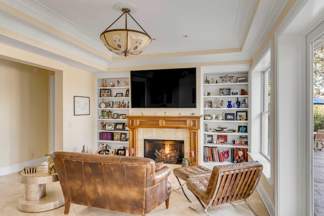 living room featuring light tile patterned floors, built in shelves, a lit fireplace, ornamental molding, and a raised ceiling