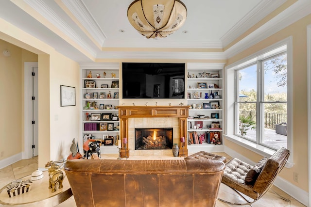 living room with built in features, a raised ceiling, baseboards, ornamental molding, and a lit fireplace