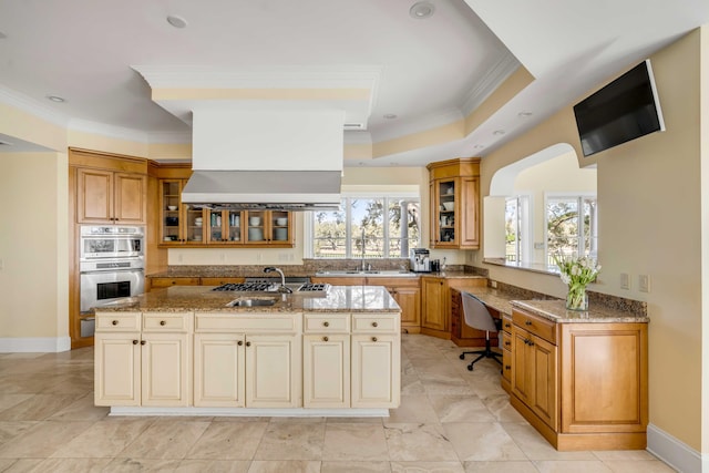 kitchen with light stone counters, glass insert cabinets, appliances with stainless steel finishes, a kitchen island with sink, and island range hood