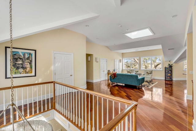 interior space featuring lofted ceiling with skylight, wood finished floors, and an upstairs landing