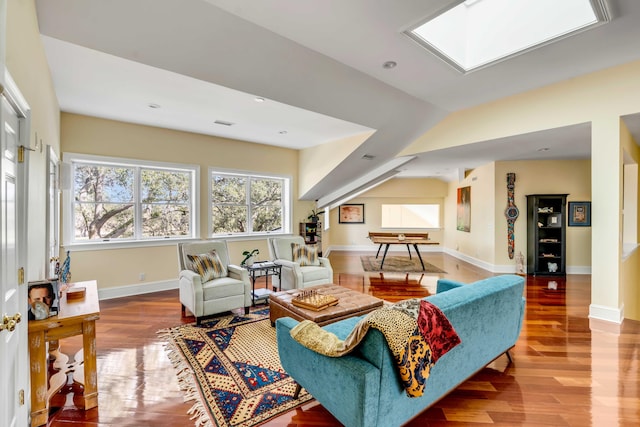 living room featuring vaulted ceiling with skylight, wood finished floors, and baseboards