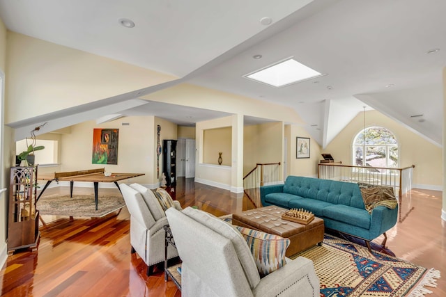 living room featuring vaulted ceiling with skylight, wood finished floors, and baseboards