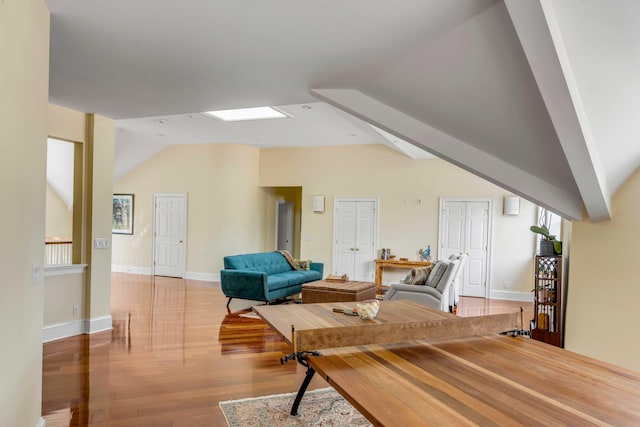 living area with lofted ceiling with skylight, baseboards, and light wood finished floors