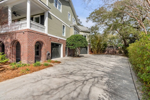 view of home's exterior featuring driveway, a ceiling fan, a balcony, an attached garage, and brick siding