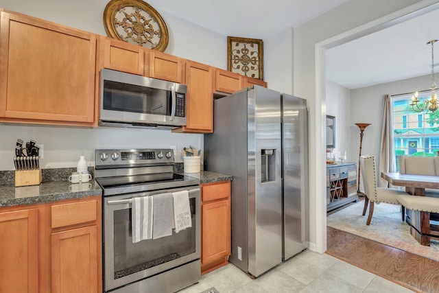 kitchen with light tile patterned floors, dark stone counters, appliances with stainless steel finishes, pendant lighting, and a chandelier