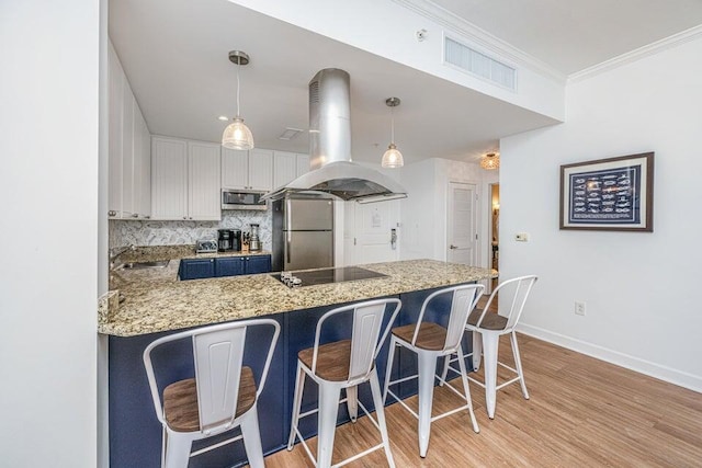 kitchen with hanging light fixtures, appliances with stainless steel finishes, white cabinetry, kitchen peninsula, and island exhaust hood