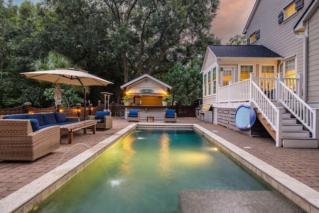 pool at dusk with a jacuzzi, a wooden deck, a patio, and an outdoor hangout area