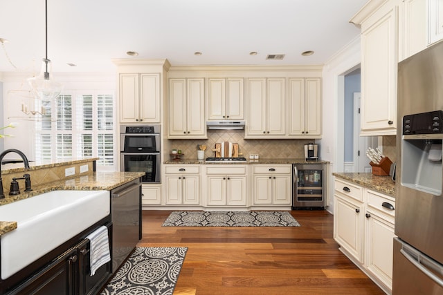 kitchen featuring pendant lighting, wine cooler, cream cabinets, and appliances with stainless steel finishes