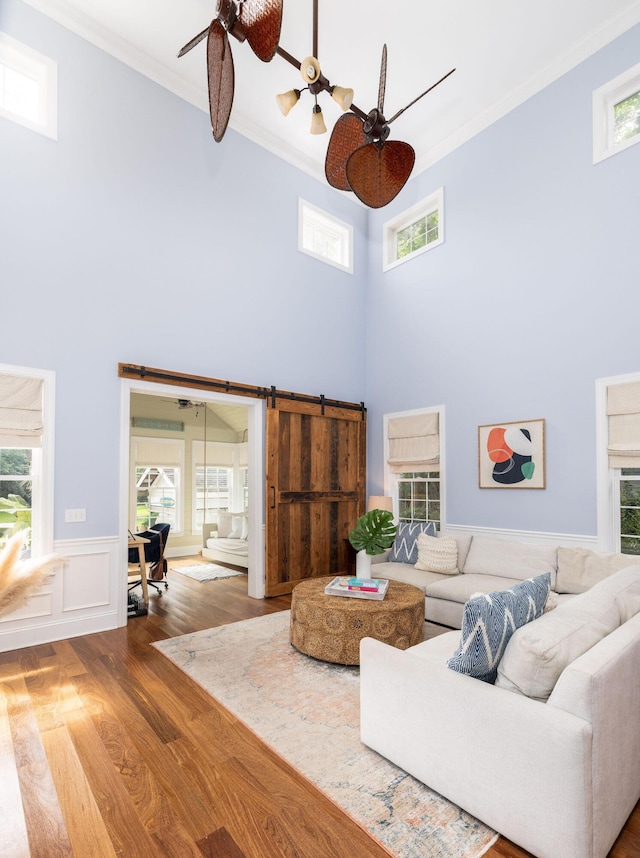 living room with a towering ceiling, wood-type flooring, crown molding, and a barn door