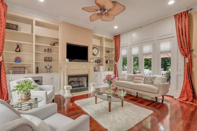 living room featuring built in shelves, a high end fireplace, crown molding, wood-type flooring, and ceiling fan