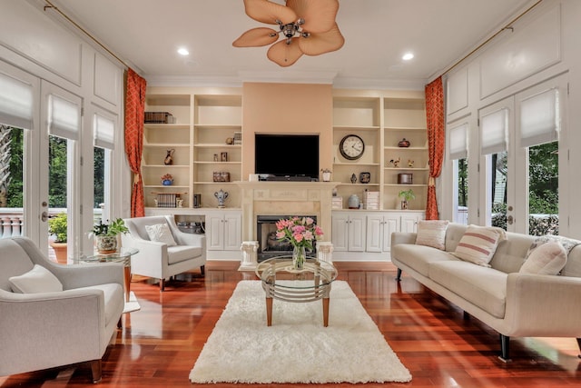 living room with built in shelves, ceiling fan, dark hardwood / wood-style floors, and ornamental molding