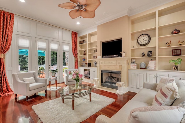 living room featuring built in shelves, ceiling fan, ornamental molding, and hardwood / wood-style flooring