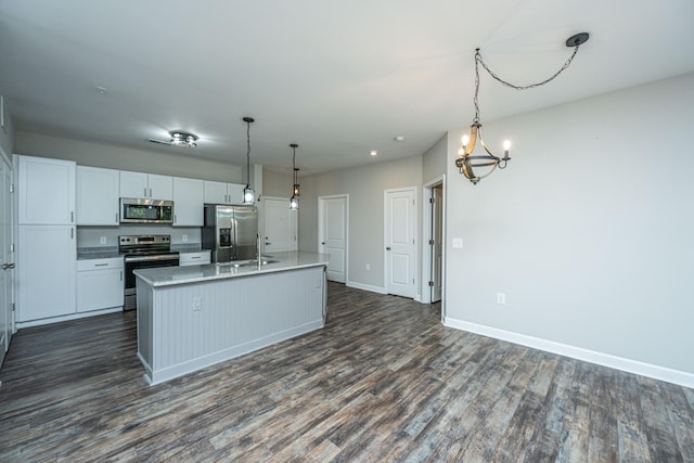 kitchen with dark hardwood / wood-style floors, pendant lighting, a kitchen island with sink, white cabinets, and appliances with stainless steel finishes