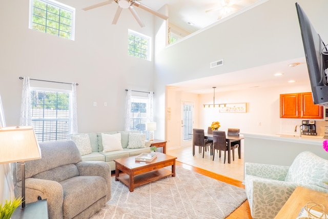 living room featuring a towering ceiling, a healthy amount of sunlight, ceiling fan, and light hardwood / wood-style floors