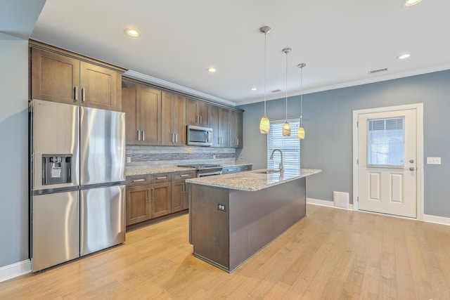 kitchen featuring a center island with sink, appliances with stainless steel finishes, light stone countertops, crown molding, and pendant lighting