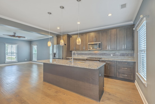 kitchen with light stone counters, hanging light fixtures, sink, light wood-type flooring, and appliances with stainless steel finishes