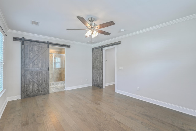 empty room with a barn door, hardwood / wood-style flooring, ceiling fan, and ornamental molding