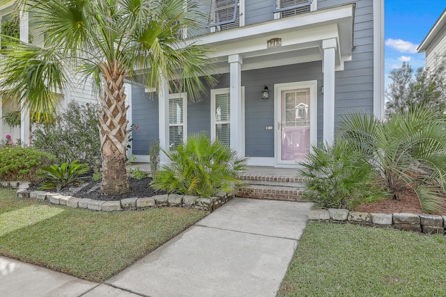 view of exterior entry featuring a porch and a lawn