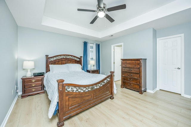 bedroom with ceiling fan, a tray ceiling, and light hardwood / wood-style flooring