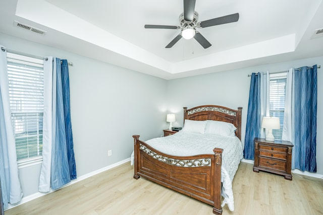 bedroom featuring ceiling fan, a raised ceiling, and light wood-type flooring